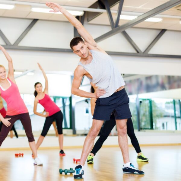 Conditioning fitness class with a male instructor leading the class in a stretch exercise