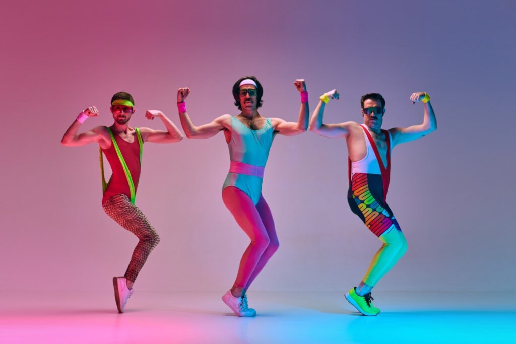 3 men dressed in spoof 80s aerobics outfits, dancing to 80s fitness music